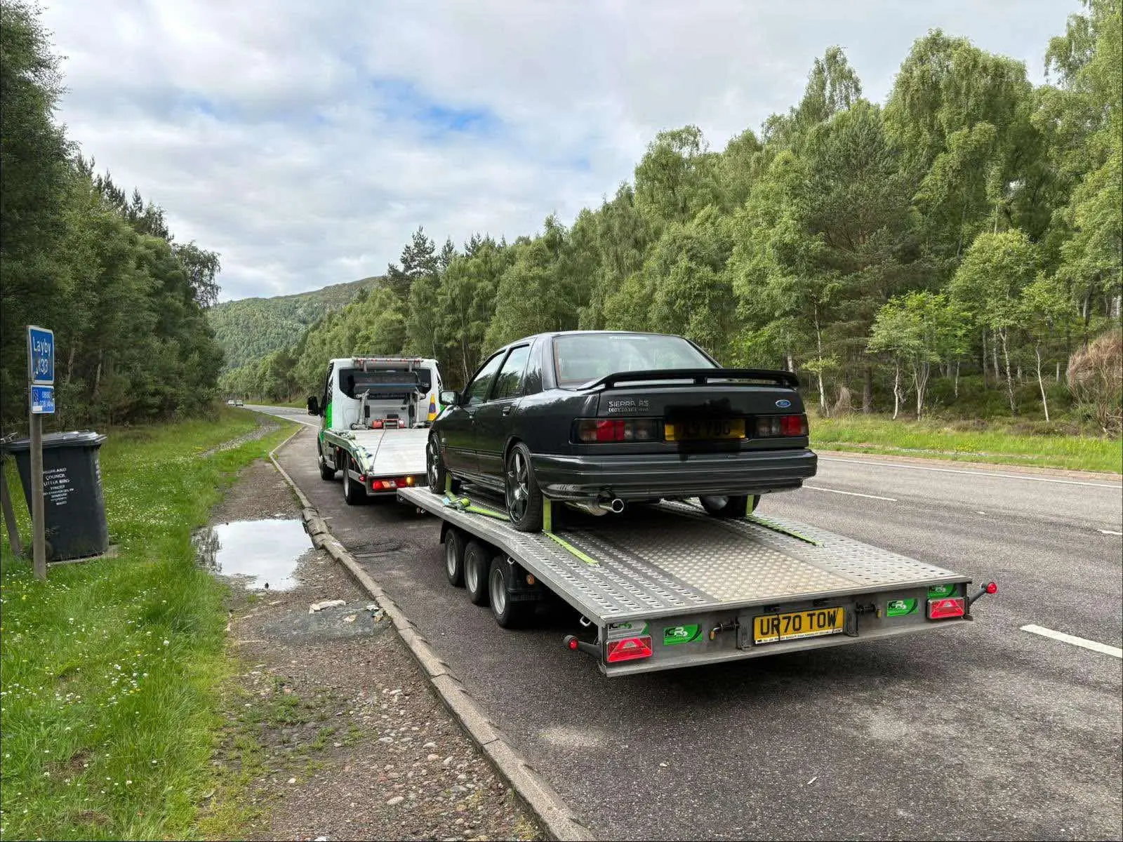 Dark car loaded onto the ICR recovery truck beside a Highland road